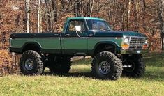 a green truck parked on top of a grass covered field in front of some trees