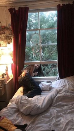 a person is sitting on a bed looking out the window at trees outside in front of them