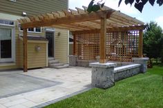 a stone bench sitting under a pergolated covered area in front of a house