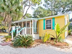 a yellow mobile home with blue shutters and palm trees in the foreground on a sunny day