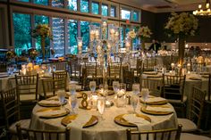 the tables are set with gold and white linens for an elegant wedding reception in front of large windows