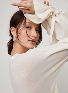 a woman with her hands on her head and wearing a white sweater over her shoulders