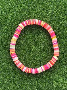 a pink, yellow and red bracelet on green grass in the shape of a circle