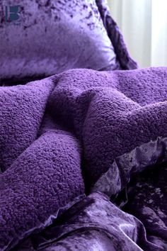 a purple comforter is laying on top of a bed with two pillows and blankets