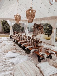 a table set up in a tent with white linens and pillows on the floor