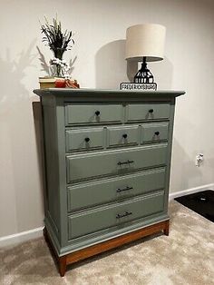 a green dresser sitting on top of a carpeted floor next to a white lamp