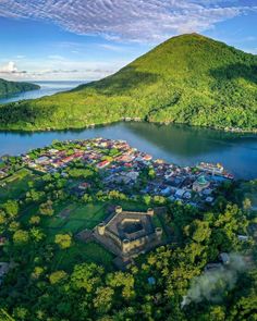 an aerial view of a small village in the middle of a lake surrounded by lush green hills