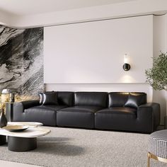 a living room with black leather couches and a marble wall behind the sofa is a round coffee table