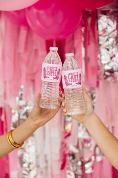 two people holding up water bottles with hello kitty labels on them in front of pink balloons