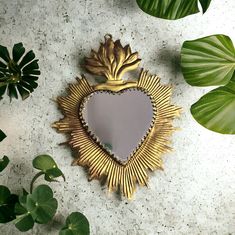 a heart shaped mirror sitting on top of a table next to green plants and leaves