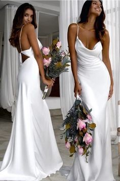 two beautiful women in white dresses standing next to each other with flowers on their bouquets