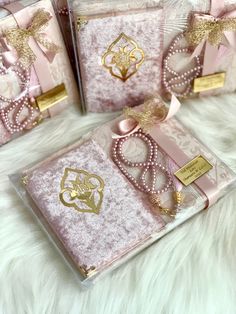 three pink and gold gift boxes with bows on them sitting on a white fur surface