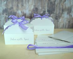 three white boxes with purple ribbons and tags on them are sitting next to each other