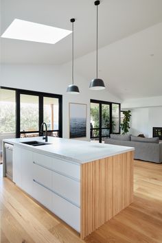 an open kitchen and living room area with wood flooring, white counter tops and black pendant lights