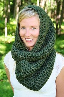 a woman wearing a green knitted cowl scarf in the woods smiling at the camera