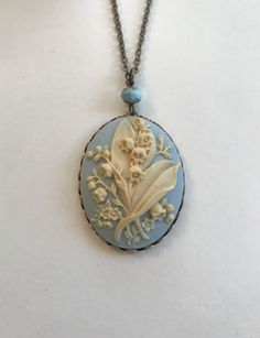 "Here is a beautiful blue lily of the valley cameo necklace. This is a large cameo which features nicely detailed lily of the valley flowers against a dreamy blue background. This cameo is set in an oxidized brass setting and is suspended from one Czech glass bead along with a high quality long brass chain. All materials are lead and nickel safe, cameo is resin. Handcrafted in the USA by Botanical Bird. This necklace comes shipped in a lovely gift box. Cameo Pendant measures: 1 1/4\" across x 1 Blue Lily Of The Valley, Lily Of The Valley Flowers, Vintage Style Necklace, Valley Flowers, Blue Lily, Vintage Inspired Jewelry, Cameo Jewelry, Cameo Necklace, Bird Jewelry