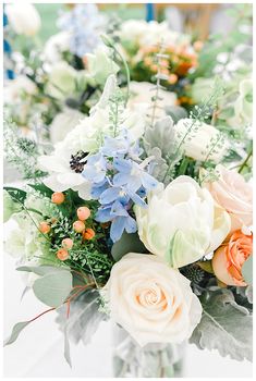 a vase filled with lots of different flowers on top of a white table covered in greenery