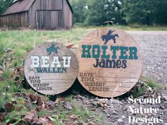 two wooden signs sitting on the ground in front of a barn and grass covered field