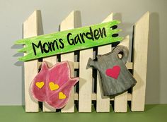 a wooden sign that says mom's garden with two flowers and a watering can