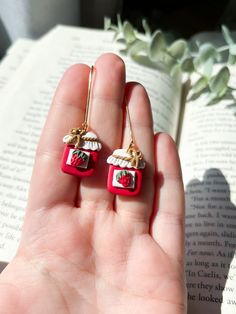 a hand holding two red and white earrings in front of an open book with flowers on it