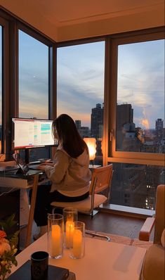 a woman sitting in front of a computer on top of a desk next to a window