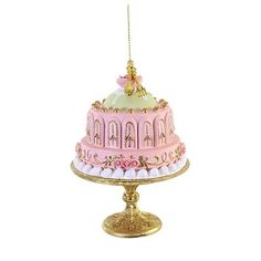 a pink and gold cake ornament hanging from a golden stand on a white background