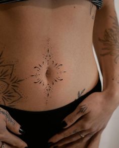 a woman's stomach with tattoos on it and her hand holding the belly area