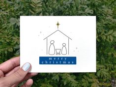 a hand holding up a christmas card with a nativity scene in the center and stars above it