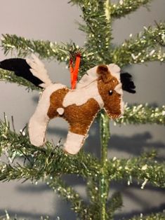 a brown and white horse ornament hanging from a christmas tree with green branches