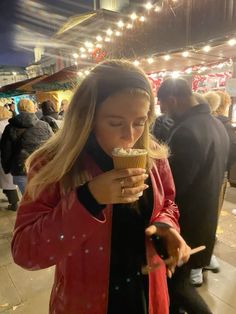 a woman eating food from a paper cup on a street corner at night with people in the background