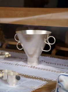 a silver cup sitting on top of a table next to other cups and spoons