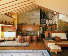 a large living room with wooden floors and stone fireplace in the center surrounded by wood paneling