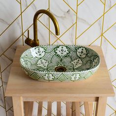 a green and white bowl sink sitting on top of a wooden table next to a gold faucet