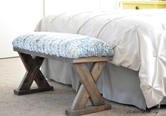 a wooden bench sitting on top of a bed next to a white sheet covered bed