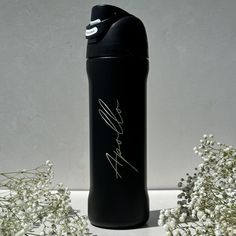 a black water bottle sitting next to white flowers