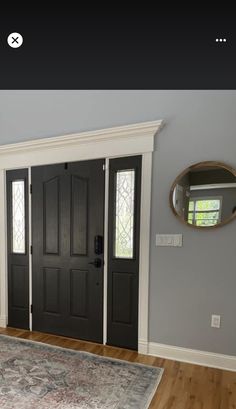 a room with a rug, mirror and two black doors