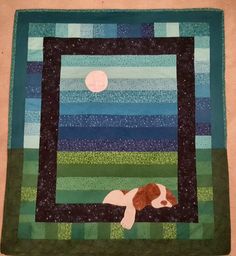 a dog is laying down on the ground in front of a blue and green quilt