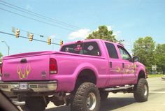 a pink pick up truck is parked on the side of the road near traffic lights