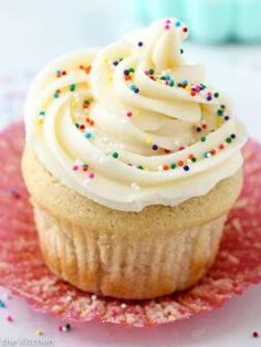 a cupcake with white frosting and sprinkles on a pink plate