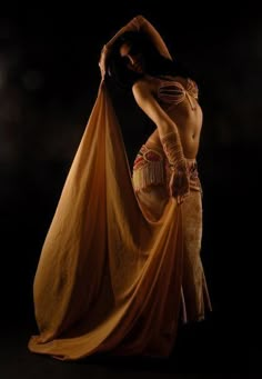 a woman in a belly dance pose with an orange cloth around her waist and hands behind her back