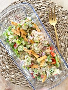 a plastic container filled with salad next to a fork on top of a woven basket