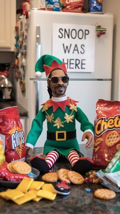 a funny snoop elf sitting with snacks around him. there is a sign on the fridge saying "snoop was here" Eclectic Kids Room, Elf Shelf, Christmas Elf Doll, Santa Costume, Buddy The Elf