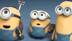 three minion toy figures are posed in front of a blue carpeted floor and one is holding a guitar