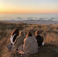 three people sitting on the ground looking out at the ocean