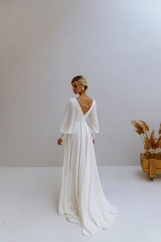 a woman in a white dress is standing next to a plant and looking at the wall