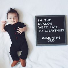 a baby laying next to a sign that says i'm the reason we're late to everything 3 months old