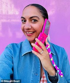 a woman holding up a pink cell phone to her ear and smiling at the camera