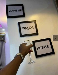 someone is holding a wine glass in front of some signs on the wall that say wake up, pray, hustle