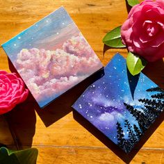 two paintings are sitting on a table next to some flowers and one is painted with acrylic paint