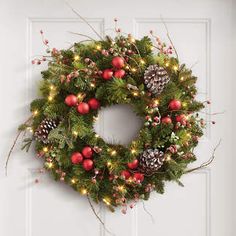 a christmas wreath hanging on the front door with pine cones and red balls around it